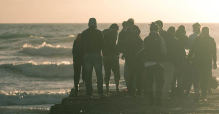 People are congregating on a breakwater watching the waves come in and standing together in community.