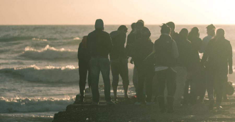 People are congregating on a breakwater watching the waves come in and standing together in community.