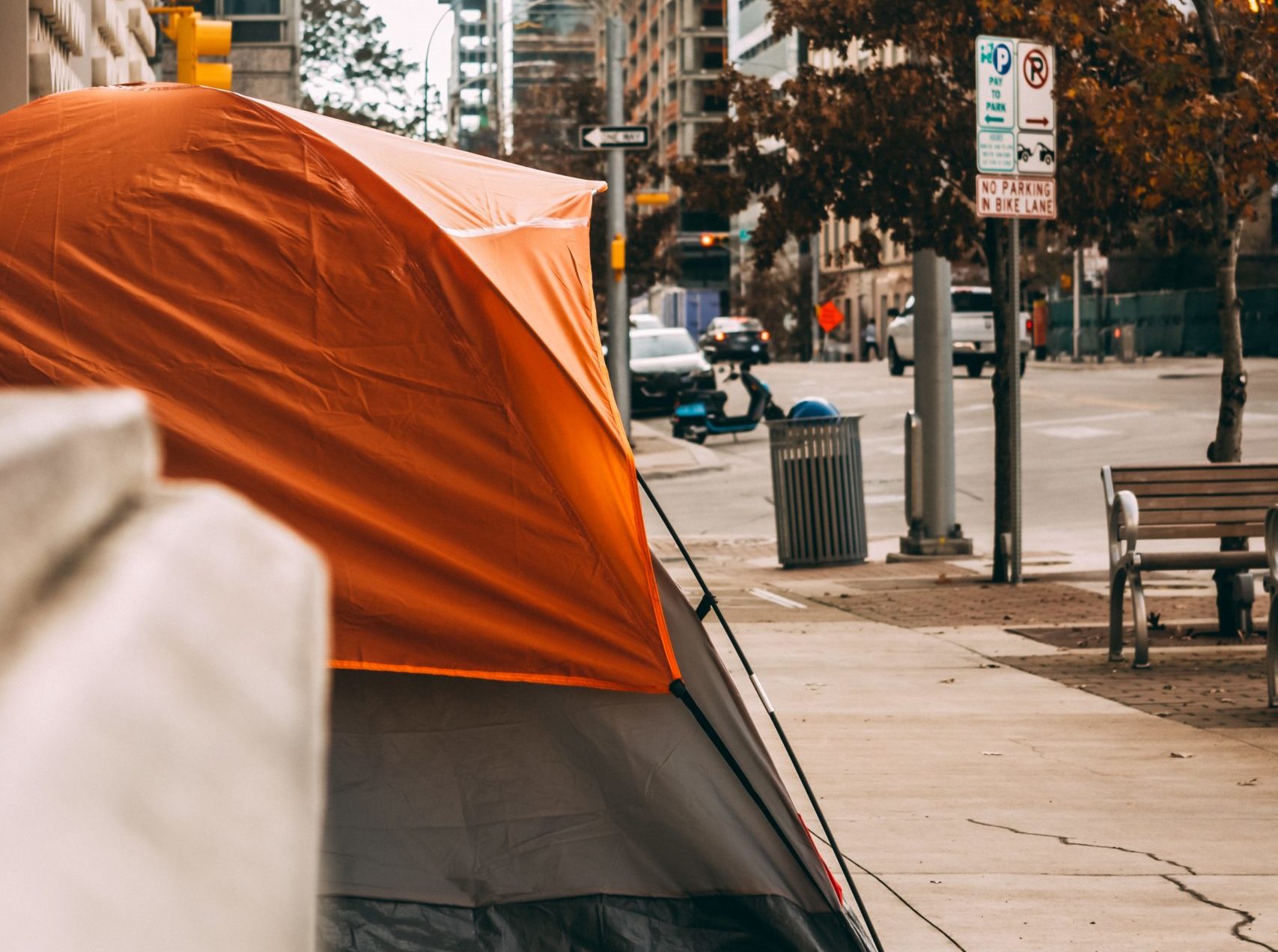Image of an orange tent set up on a sidewalk, downtown in a city.
