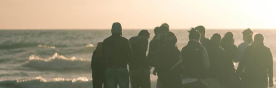 People are congregating on a breakwater watching the waves come in and standing together in community.